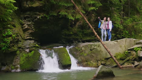 un par de jóvenes turistas están de pie cerca de una cascada en un río de montaña admirar la hermosa sc