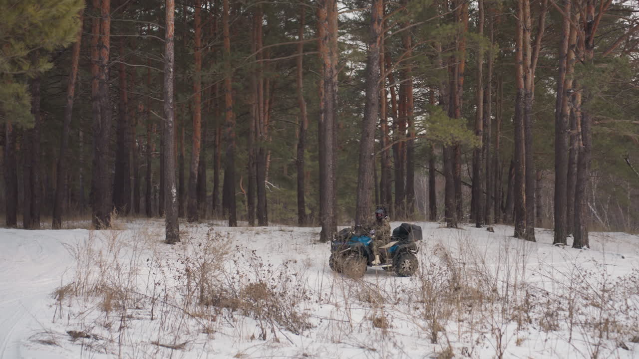 Un quad riposa in un boschetto di pini innevato. Veicolo silenzioso parcheggiato tra alberi innevati e aria fredda. Radura coperta di neve dove un ATV rimane inattivo in un boschetto di pini ghiacciato sotto un cielo grigio.