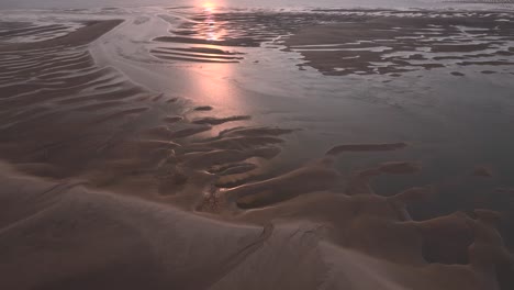 sunset on sand patterns and pool reflections at low tide on tidal sand banks. reverse flight over.
