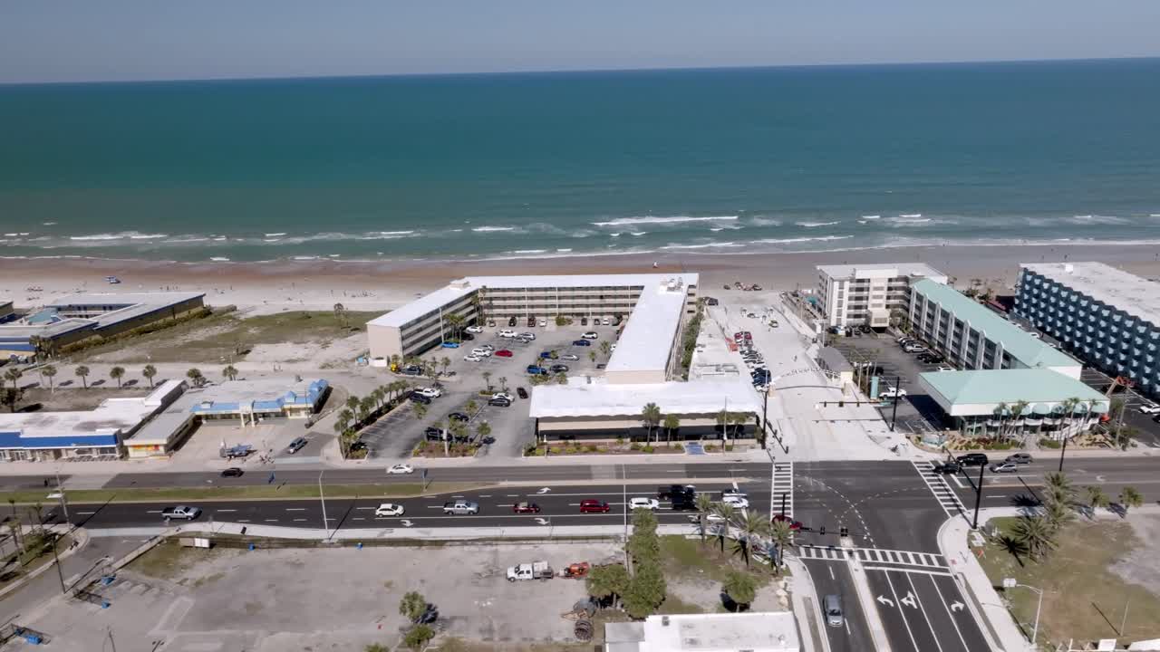 Daytona Beach, Florida with waves from the Atlantic Ocean, vehicles, hotels and people on the beach with drone video moving left to right.