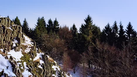 Drone-flight-close-to-a-volcanic-hilltop-in-winter-revealing-a-natural-forest-and-a-snowy-plateau