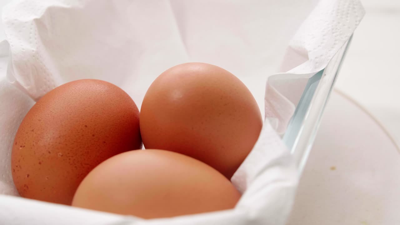 Three organic fresh eggs in a rotating container on white wrapping paper for making food