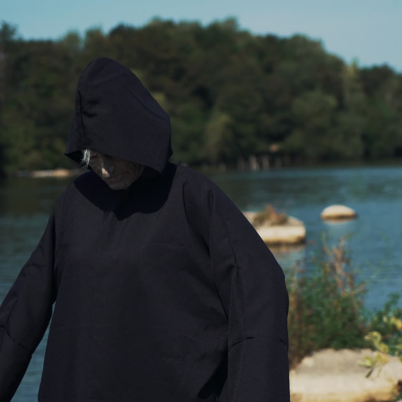 Eerie witch on river bank watches the camera. Halloween costume.