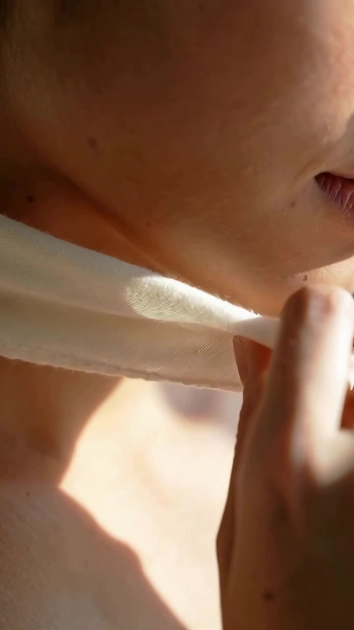Video verticale: Mani che entrano nell'inquadratura, una donna sistema una sciarpa leggera alla finestra per lisciare il tessuto.