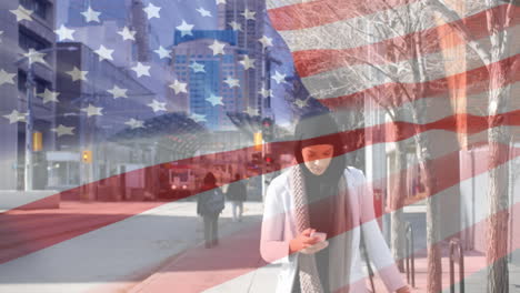 animation of american flag waving over biracial woman in hijab using smartphone
