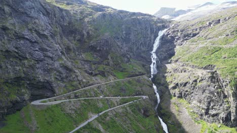 trollstigen mountain road in norway - cars drive touristic route with scenic waterfall and hairpin turns - aerial circling