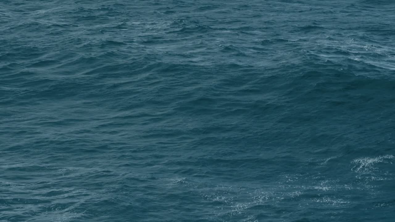 Cinematic aerial shot of dark blue ocean surface, moody sea waves, deep ocean