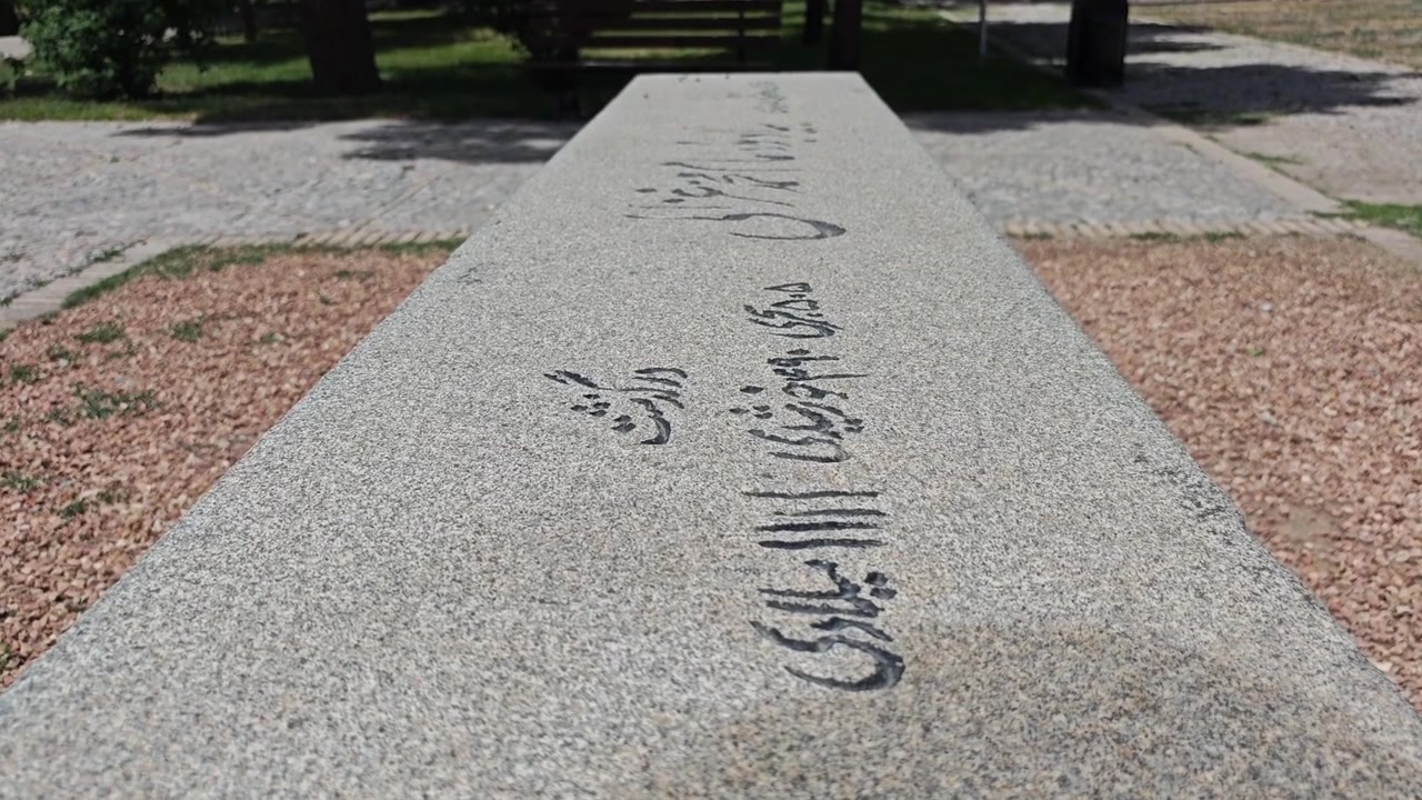 Primo piano di una panchina in pietra con calligrafia persiana in un parco pubblico