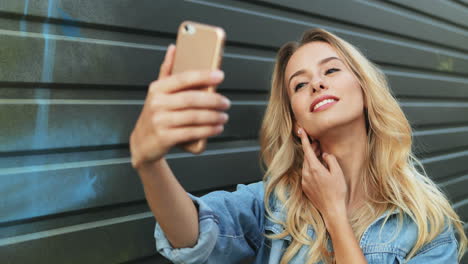 young caucasian blonde woman in jeans jacket taking a selfie on the smartphone in the street