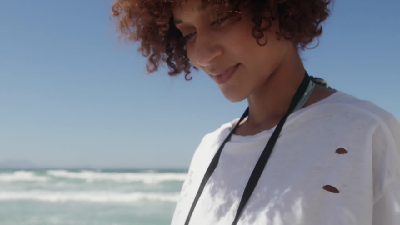 Front view of African american woman using mobile phone on the beach 4k