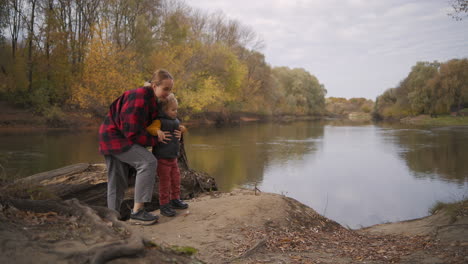 happy mother and her little child are walking together at autumn park with river breathing fresh fall air and enjoying nature family rest at weekends