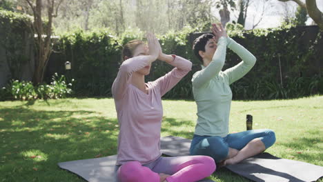 Happy-caucasian-lesbian-couple-practising-yoga-in-sunny-garden,-slow-motion