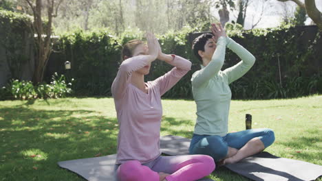 una feliz pareja de lesbianas caucásicas practicando yoga en un jardín soleado, en cámara lenta