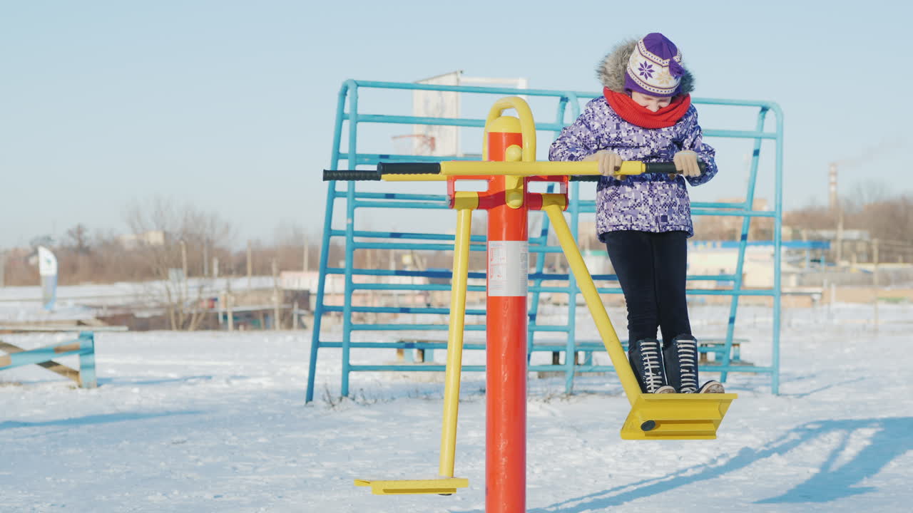 una niña con ropa abrigada está jugando en el patio de la escuela montando un entrenador de fitness