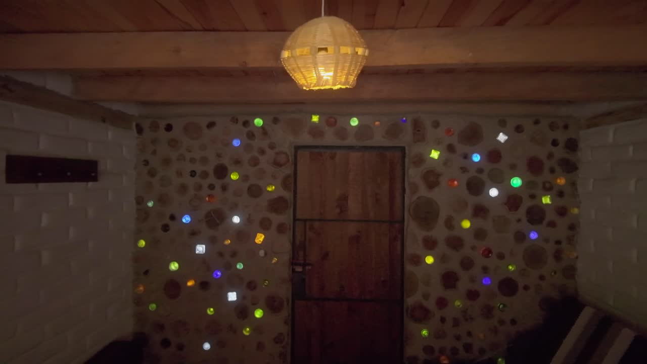 Dolly-in view of colorful cob wall with embedded bottles and wooden door in rustic superadobe home. Dolly in