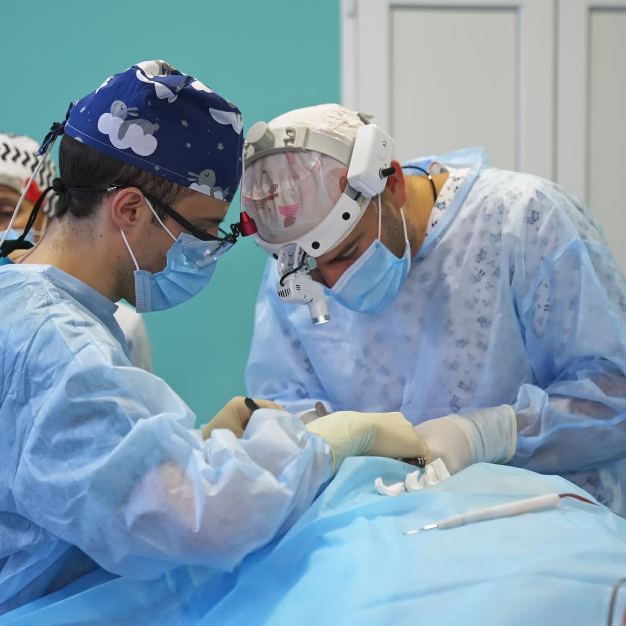 Focused surgeons use metal tools at operation. Two professionals working simultaneously on one patient. Female medic at backdrop