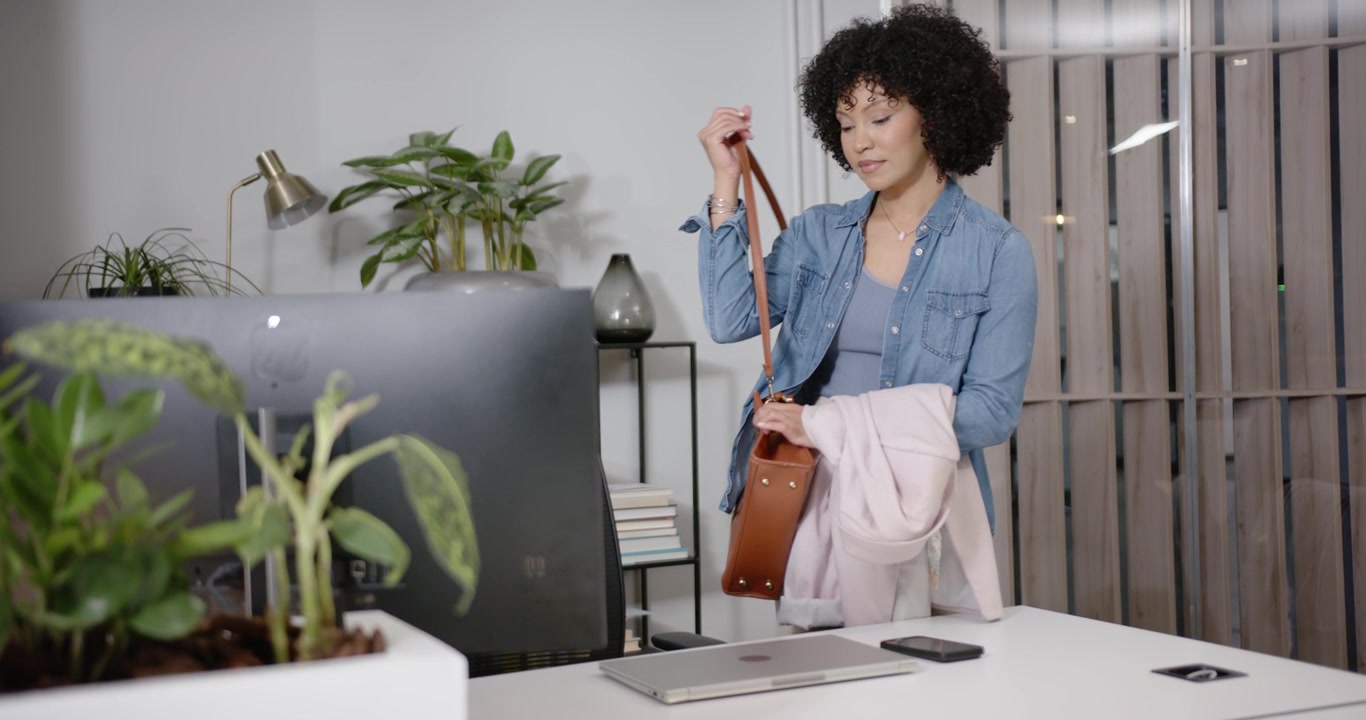 African female entering, placing laptop, phone, fixing jacket and bag at office desk preparing work