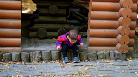 lovely two-year-old baby boy sitting peacefully on the threshold of wooden pavilion. cute kid stands up and runs up to camera.