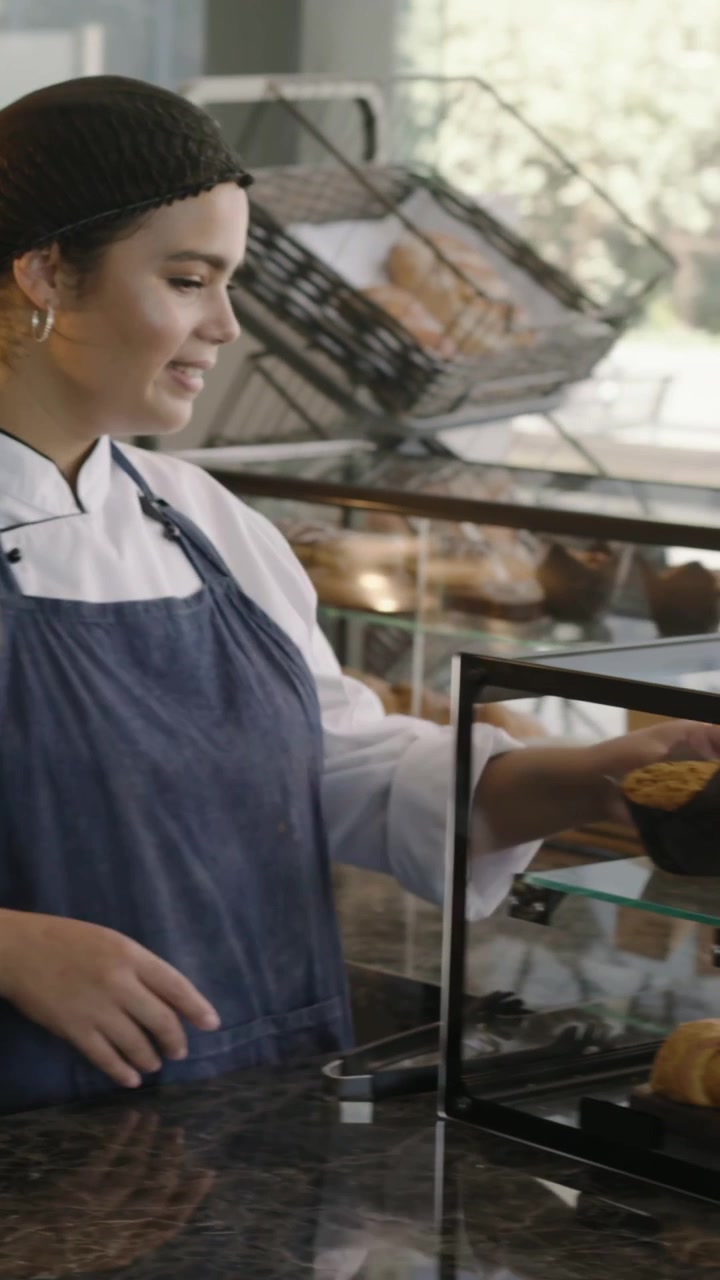 Video verticale: Cliente che si avvicina al bancone, con il fornaio in grembiule che serve un dolce e usa il POS, spazio per il testo.