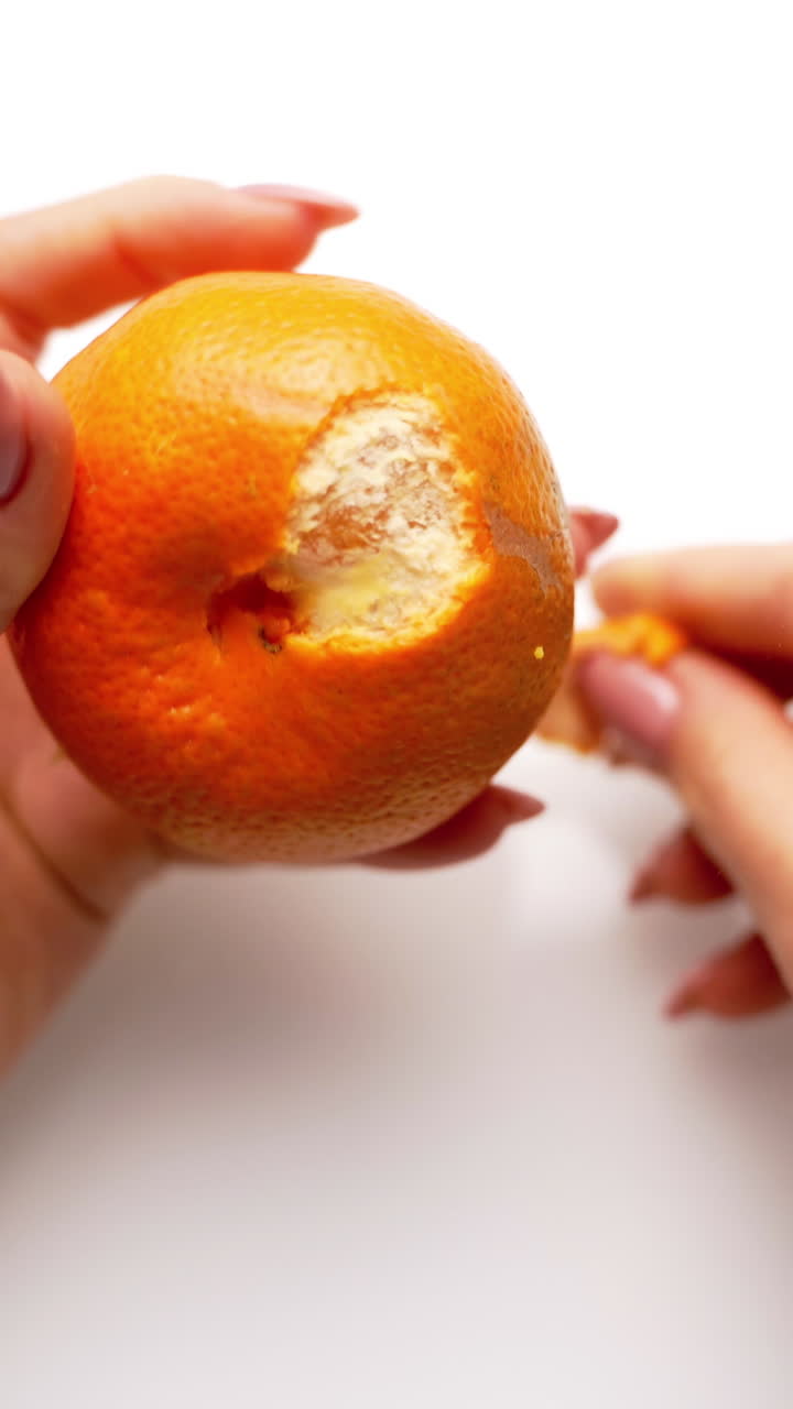 Woman cleans tangerine on the table. Top view of female's hands holds sweet citrus. Hands are peeling fresh mandarin. Close-up. Vertical video