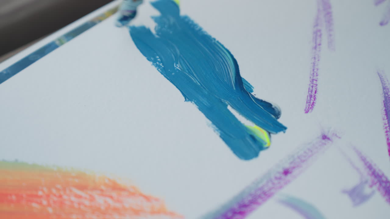 close up painter hand painting blue strokes on textured white paper with watercolor brush beside orange backdrop strokes showcasing dynamic artistic process and vivid color contrast