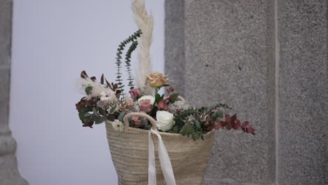 Rustic-basket-filled-with-roses,-greenery,-and-pampas-grass-against-a-stone-wall-background