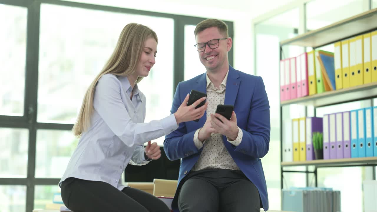 Happy Colleagues Sharing Moments on Smartphones in Office