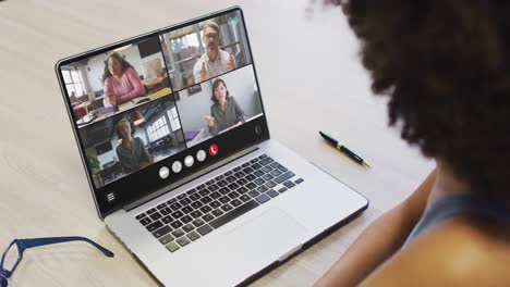 mujer afroamericana usando una computadora portátil para una llamada de video, con diversos colegas de negocios en la pantalla