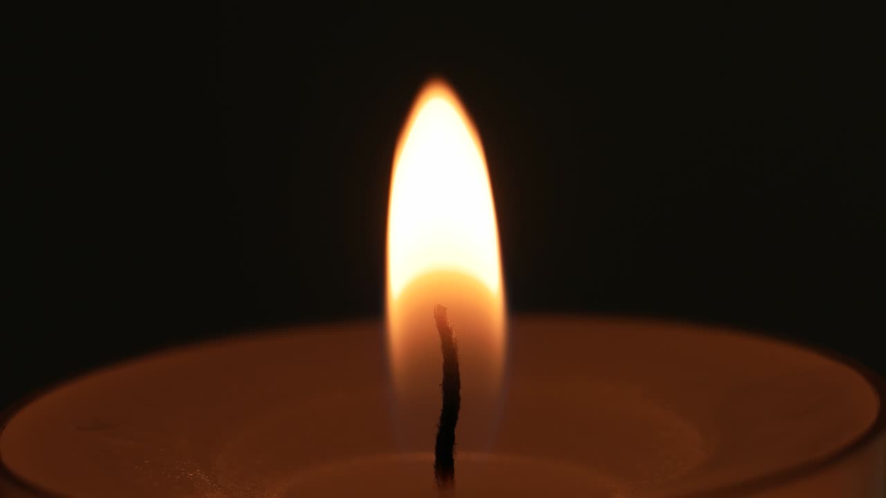 Una singola piccola candela bianca che brucia. Primo piano in studio, isolata su sfondo scuro.