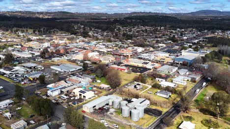 drone footage glides above coonabarabran, nsw, revealing residential streets, commercial buildings, and green spaces under bright daylight with steady camera movement