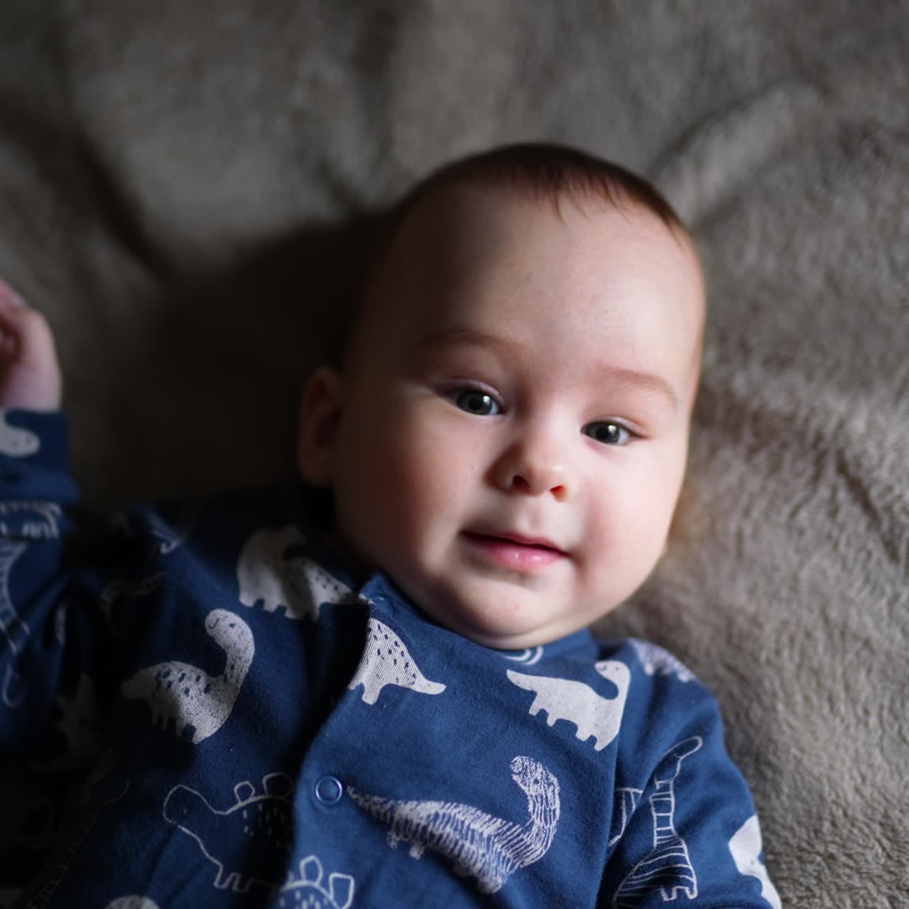 Beautiful toddler boy lies on bed looking into camera with interest. Sweet child upper body part close up