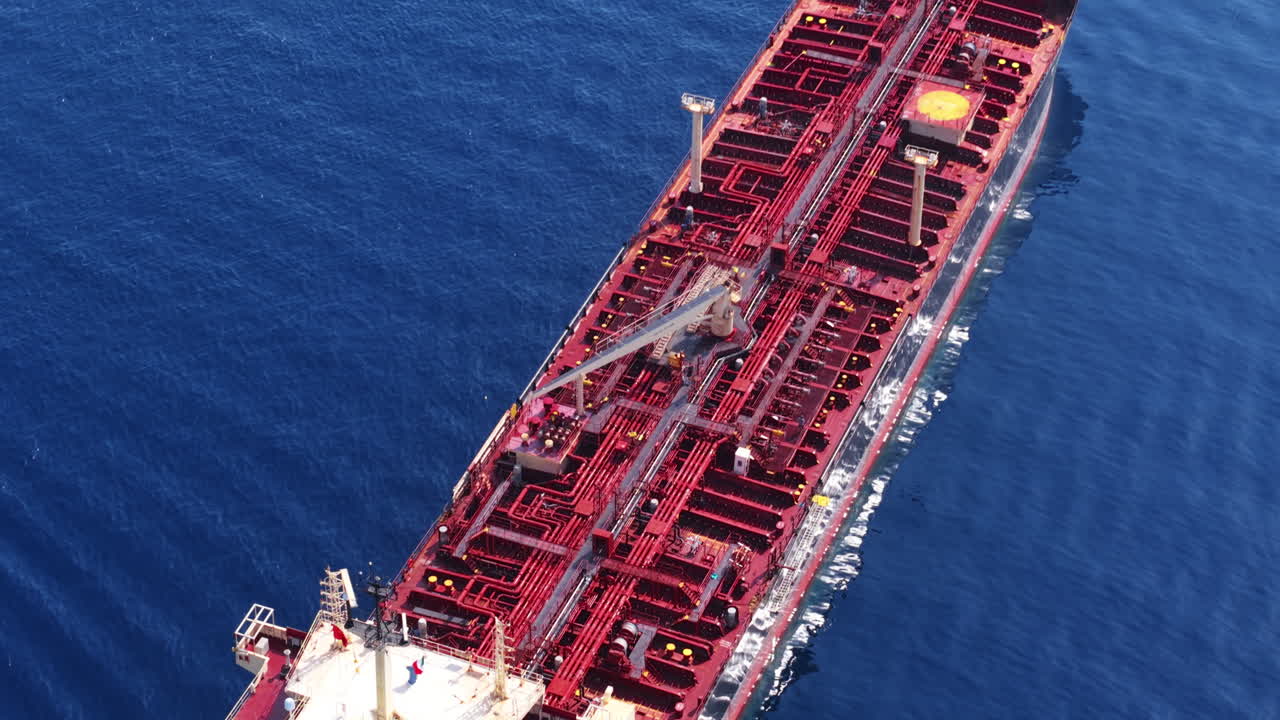 Drone starts in top-down view on oil tanker, then tilts up to reveal entire red ship surrounded by blue sea in Sicily