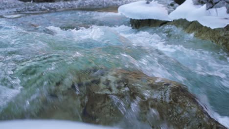 emerald river water at the winter time flowing through rocks under snow, slow motion