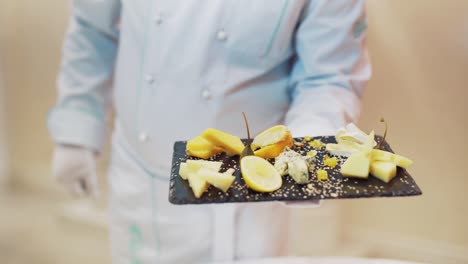 serving different types of hard cheese with lemon and sesame on the background of black wooden board in the cafe. close-up.