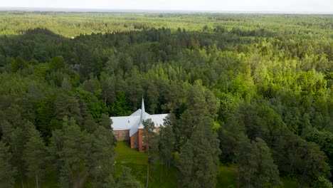 gorgeous aeral drone footage orbiting and spinning around and old vintage and historic red brick church during summer time when clouds are creating shadows from the sun on the treetops at alatskivi