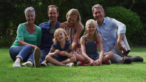 portrait of smiling caucasian parents, grandparents and grandchildren sitting in garden smiling