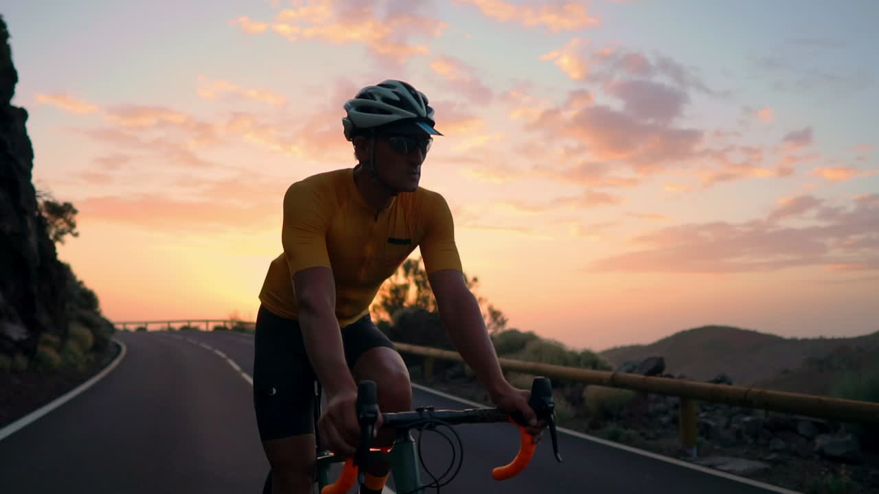 Slow motion captures the athlete navigating a mountain serpentine on a bike, taking pleasure in the island's view, representing a commitment to a healthy lifestyle at sunset