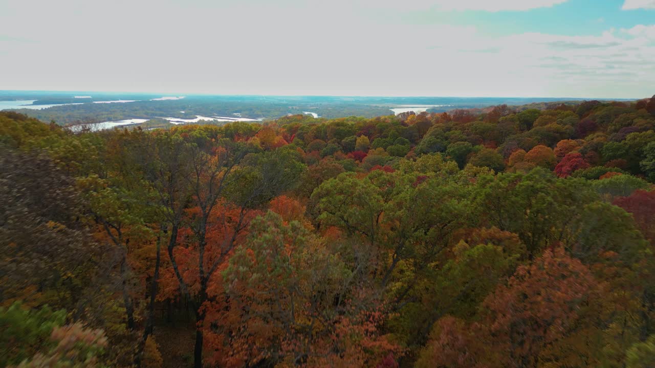 A shot coming up over a wooded hillside revealing the Mississippi River Valley under a sunny blue sky. The forest is colorful with peak autumn foliage.