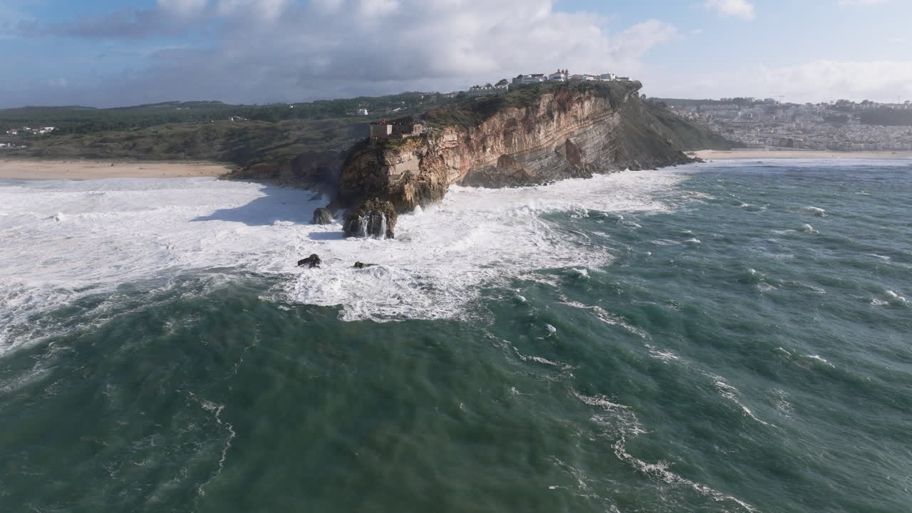 Aerial drone shot of big waves breaking on rocks and cliffs on a day with giant waves in Nazaré, Portugal, Europe. Farol da Nazaré lighthouse