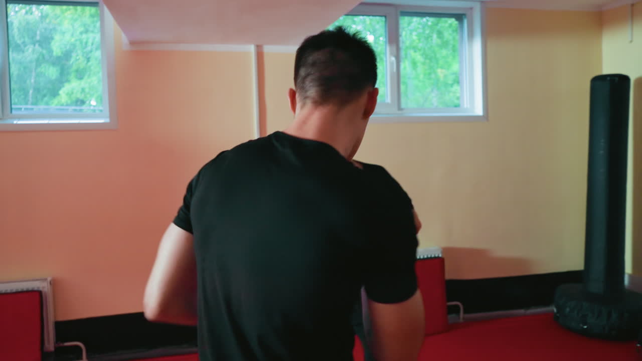 Fighters training in gym, young man in red gloves squaring off against opponent in black gloves, focusing on technique, stance, and concentration during sparring session