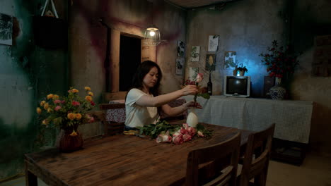 woman trims flowers at a table and places them in a vase