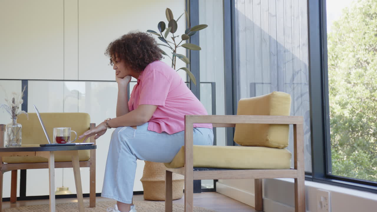 Working on laptop, plus size woman sitting in modern living room, focused