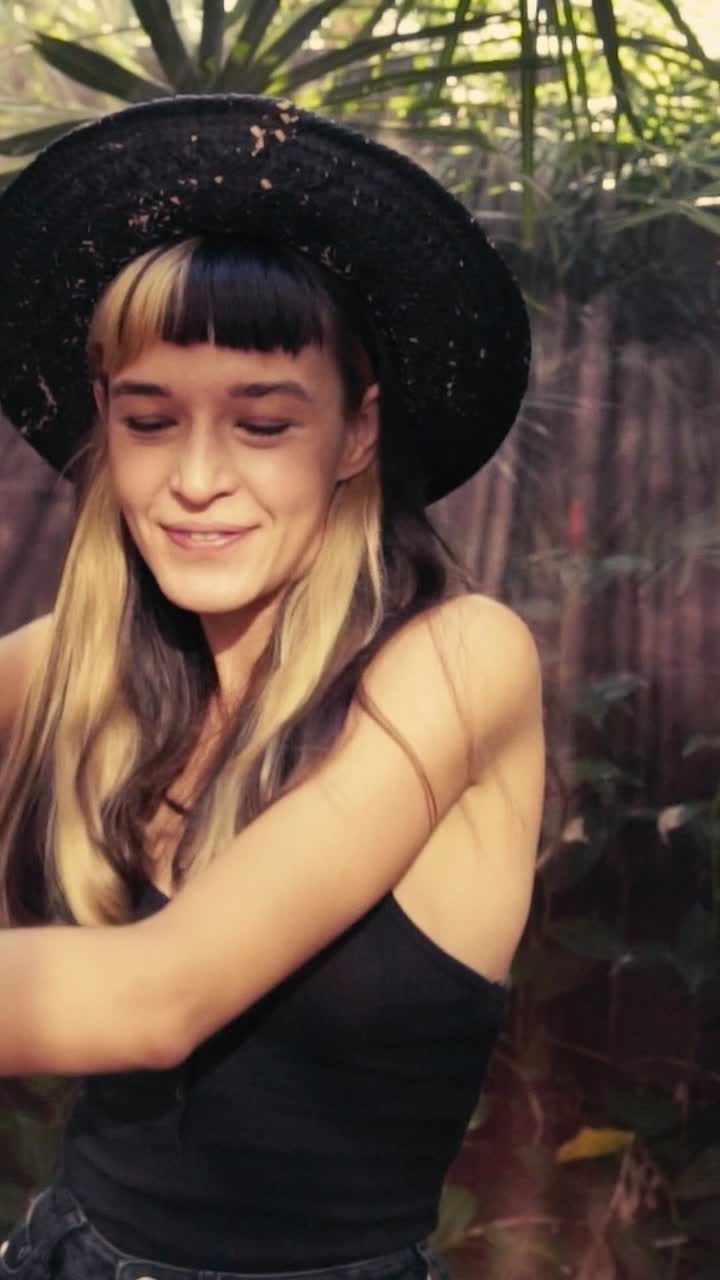 Young caucasian woman slowly waves smoke bomb and smiles stands in jungle