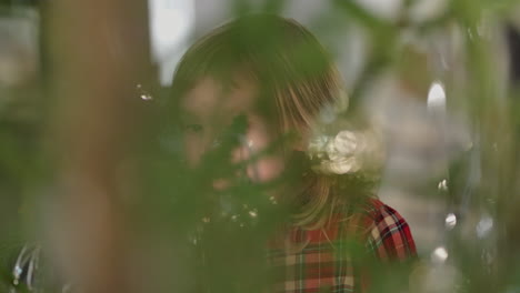 little girl can be seen through the christmas tree, quietly excited with anticipation, as the family decorates