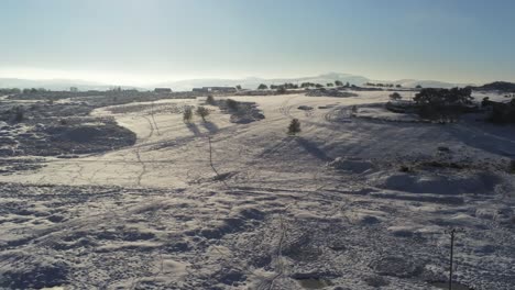 Snow-covered-rural-winter-countryside-track-footprint-shadows-wilderness-rising-aerial-view