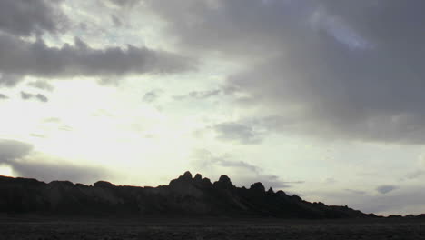 Wispy-gray-and-white-clouds-pass-over-a-mountain-summit-at-golden-hour