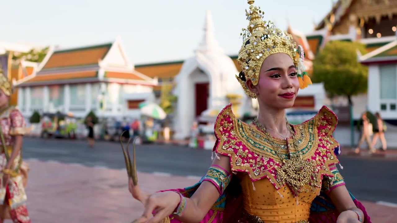 Uma dançarina tailandesa em traje dourado ornamentado executa movimentos tradicionais fora de um templo em Bangkok