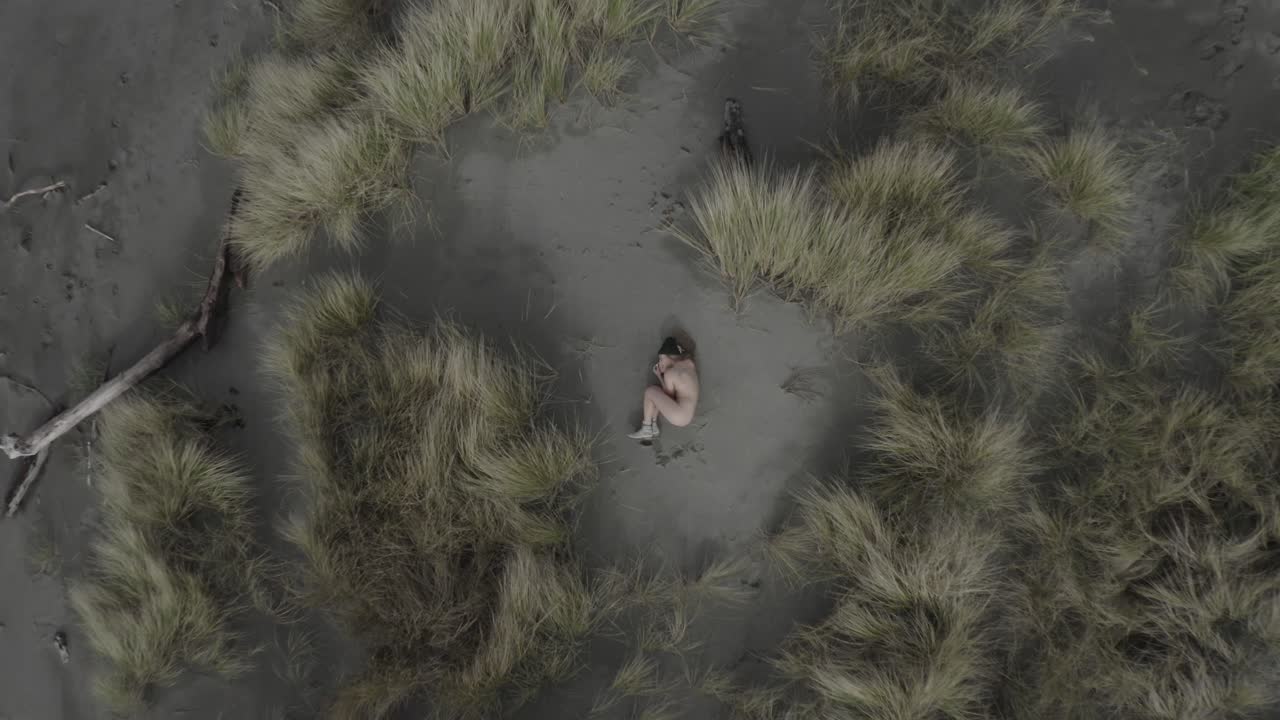 해변에 몸을 웅크리고 있는 벌거벗고 문신을 한 여성의 멋진 공중 촬영