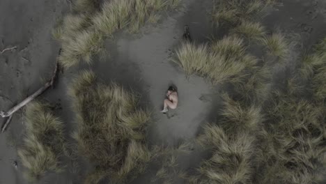 Excelente-Toma-Aérea-Alejándose-De-Una-Mujer-Desnuda-Y-Tatuada-Acurrucada-En-La-Playa