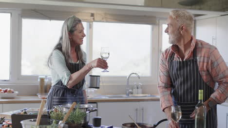 middle aged caucasian couple drinking wine, preparing meal, cooking in kitchen at home, slow motion